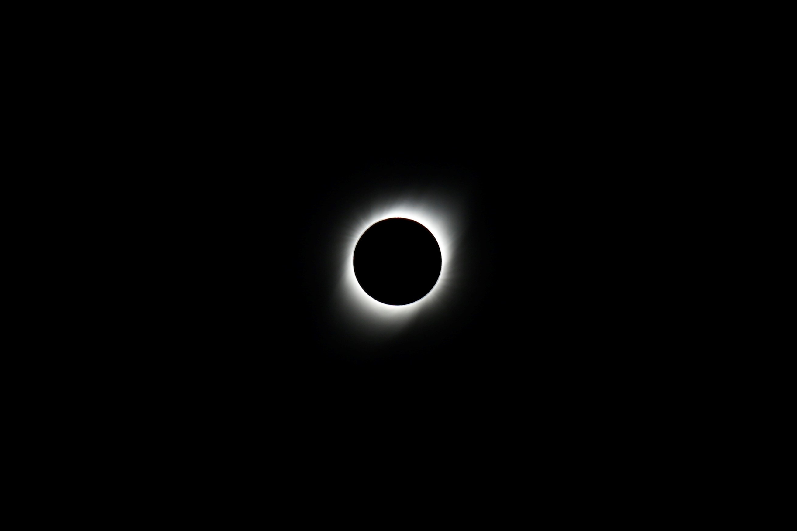 The sun, a black circle obscured by the moon and surrounded by a glowing white corona, hangs in a black sky.