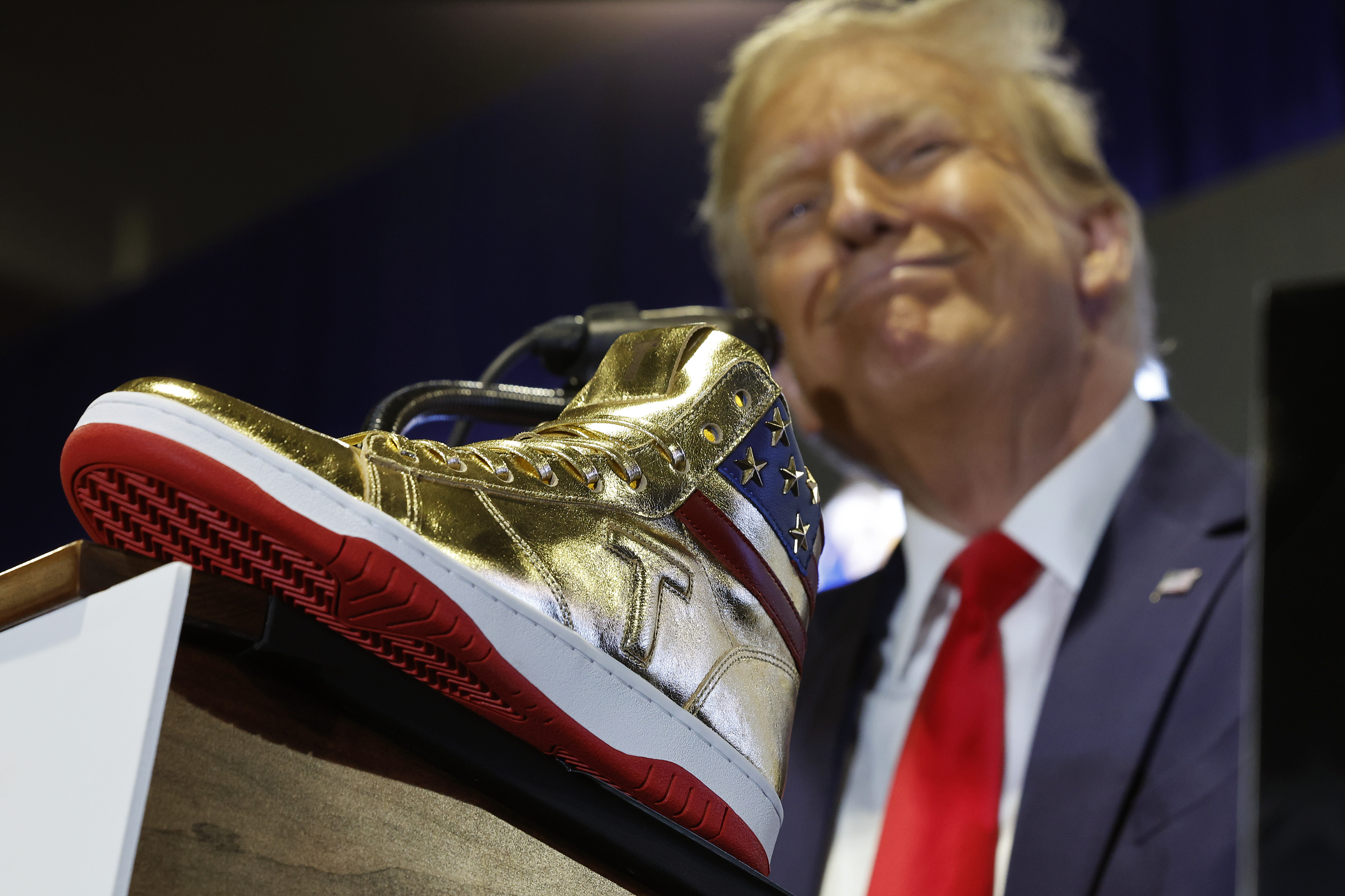 A close-up of a gold high-top sneaker with Donald Trump smirking in the background.