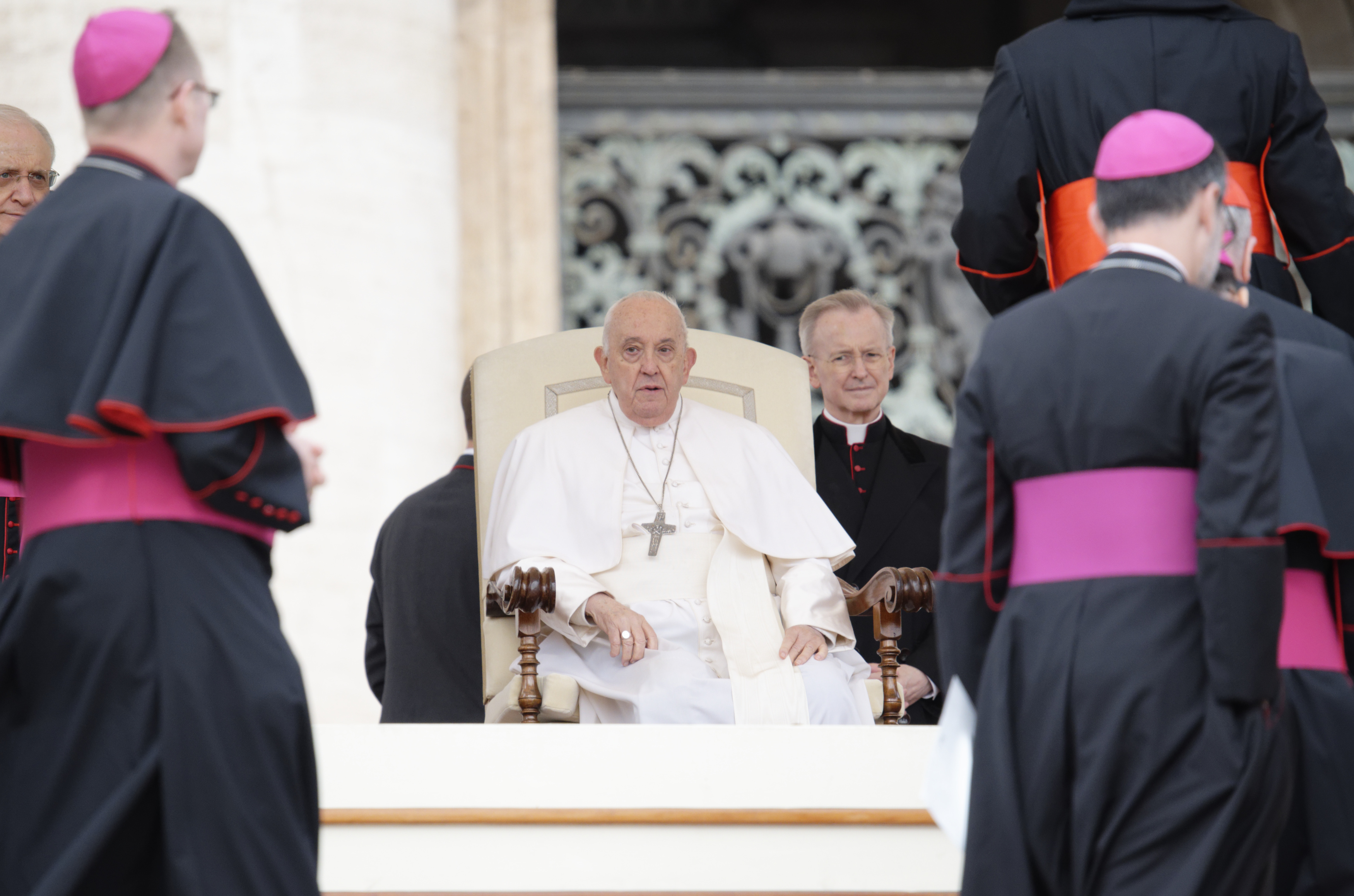 Bishops pass by Pop Francis, who is sitting in a large chair.
