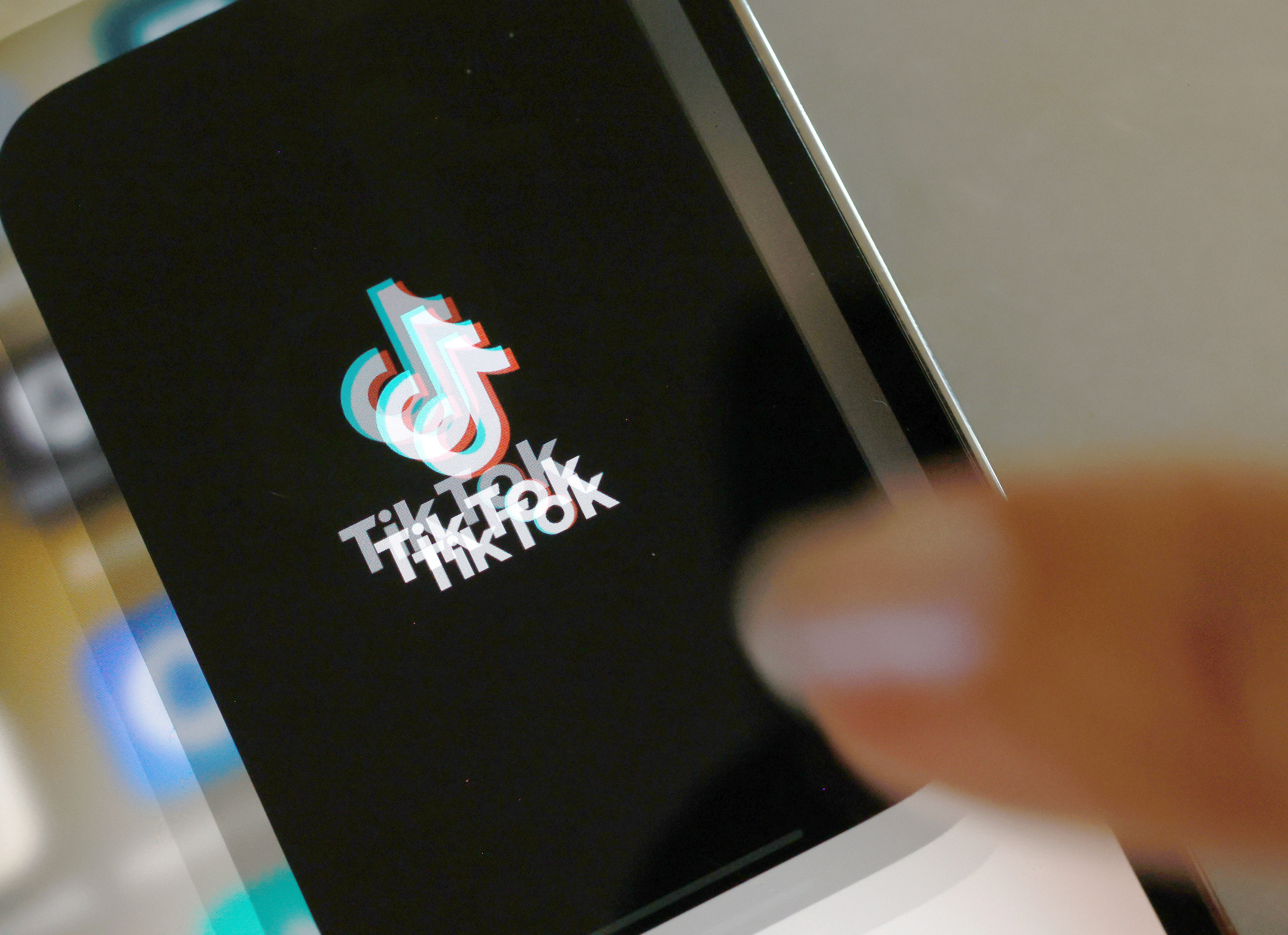 A photo illustration of the TikTok app, displayed on a phone screen. The logo is blurred as if from rapid movement.