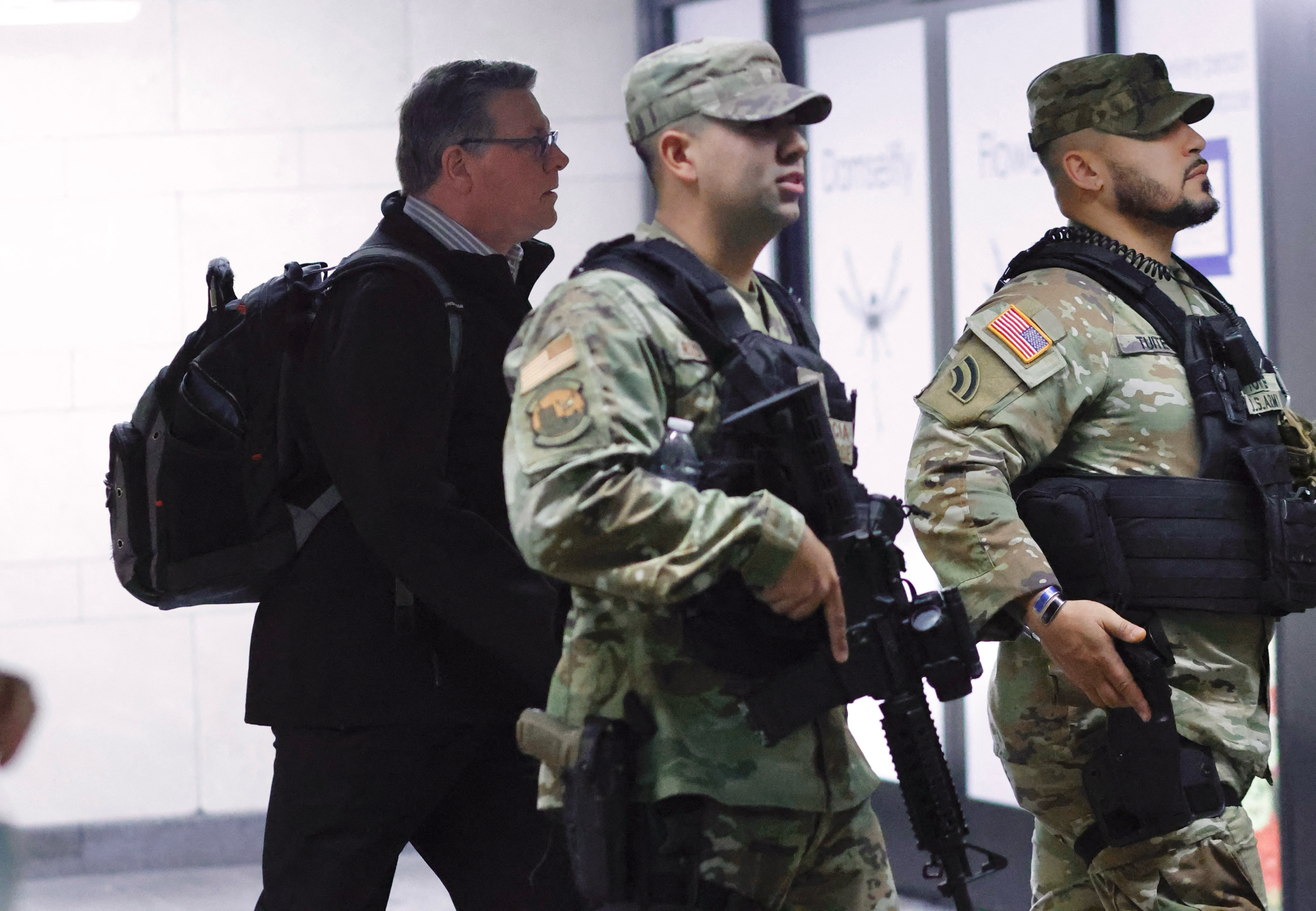 Two national guard troops in uniform patrolling a subway station with a commuter in the background.