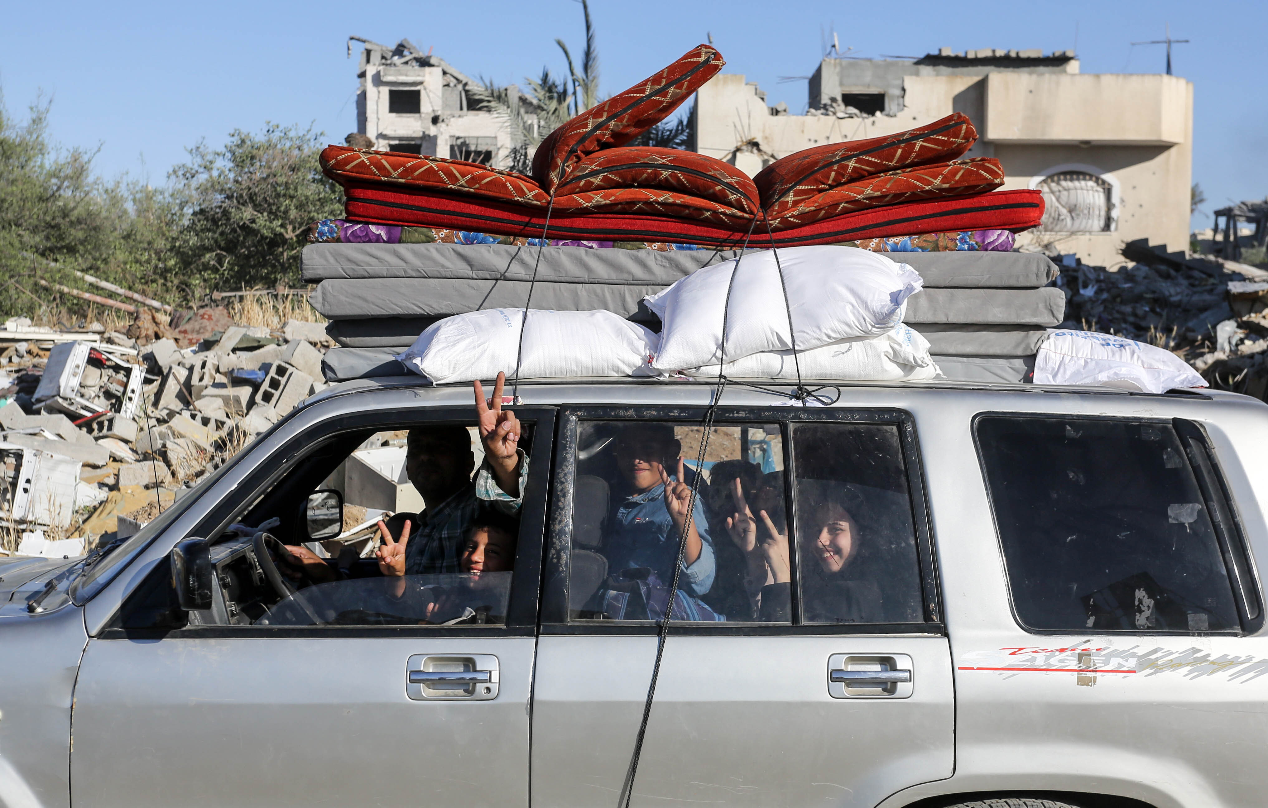 Palestinians in a packed car with mattresses stacked on top.