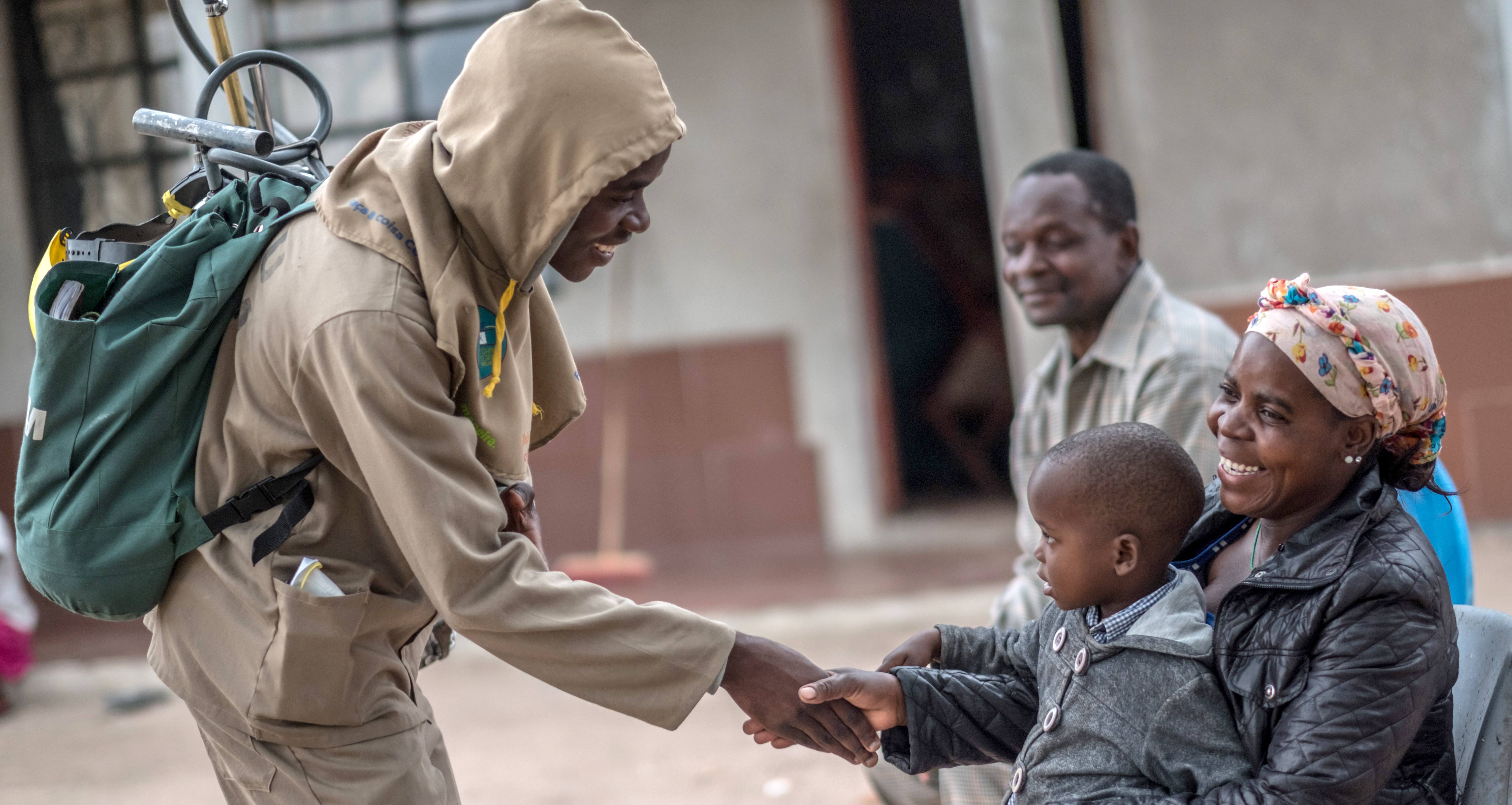 A health worker carrying insecticide sprayer is shaking hands with a boy in Mozambique.