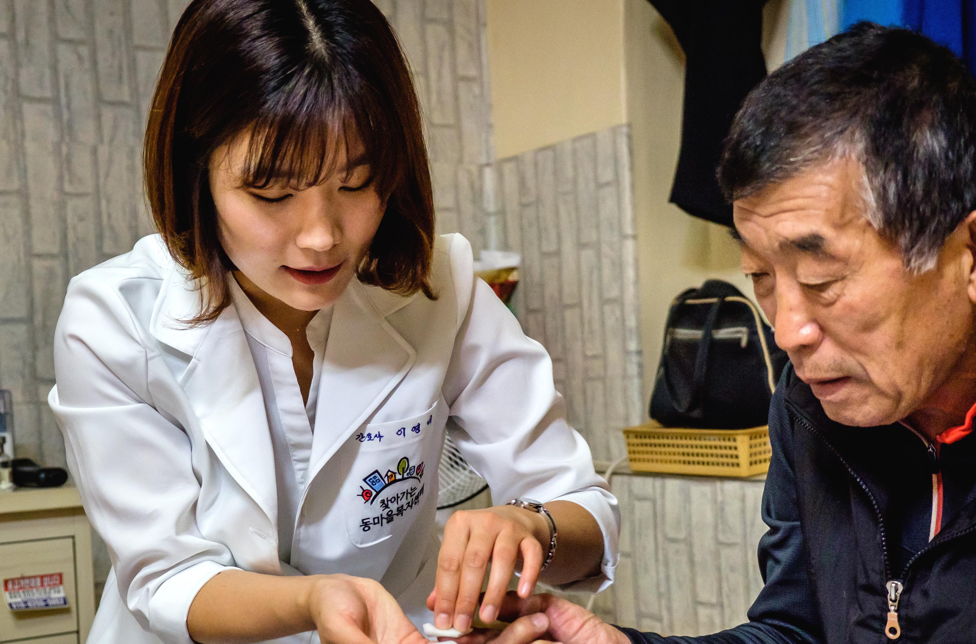 A visiting nurse from Seongbuk Home Health Care Center is checking a man's blood sugar and educate him on the harmful effects of smoking during a home visit