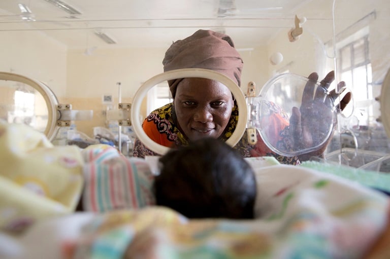 Mother watching her baby from outside of an infant incubator.