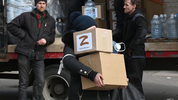 Жительница города несет коробки с гуманитарной помощью 
