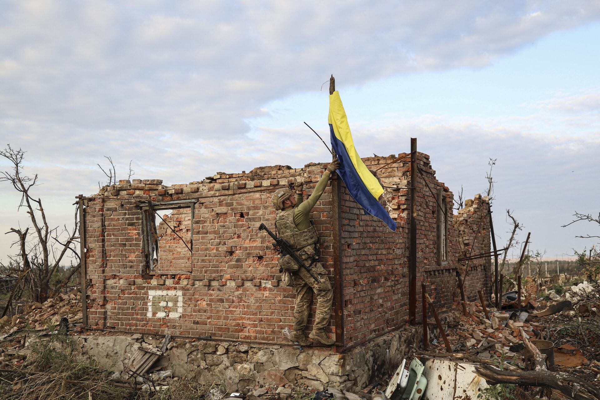 Военнослужащий подразделения ВСУ поднимает украинский флаг над ранее разрушенным зданием - РИА Новости, 1920, 13.12.2023