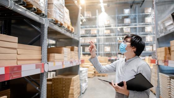 wearing face mask doing stocktaking of product in cardboard box on rack in warehouse