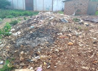 Route de terre bordée de débris et d’ordures près d’habitations, signe d’un manque de gestion des déchets