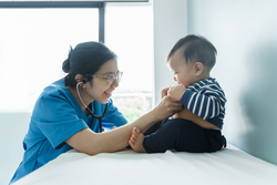 Cheerful Chinese or Japanese woman Doctor playing with her little patient, Asian Female pediatrician examining baby boy with stethoscope in medical examination room. BeH3althy