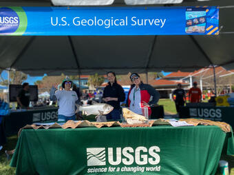 Three UGSS staff smiling at a table with various animal displays under a tent