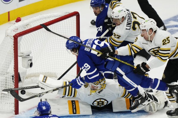 Boston Bruins goaltender Jeremy Swayman (1) makes a save on Toronto Maple Leafs' Tyler Bertuzzi (59) as Bruins' Hampus Lindholm (27) and Brandon Carlo (25) defend and Maple Leafs' Auston Matthews (34) looks on during the third period of action in Game 3 of an NHL hockey Stanley Cup first-round playoff series in Toronto on Wednesday, April 24, 2024. (Frank Gunn/The Canadian Press via AP)