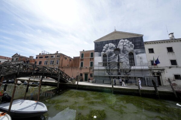 The installation '"I piedi, insieme al cuore, portano la stanchezza e il peso della vita" ('The feet, together with the heart, carry the tiredness and weight of life') by Italian artist Maurizio Catalan is displayed on the facade of the church next to the women's prison at the Giudecca island during the 60th Biennale of Arts exhibition in Venice, Italy, Wednesday, April 17, 2024. A pair of nude feet dirty, wounded and vulnerable are painted on the façade of the Venice women's prison chapel, the work of Italian artist Maurizio Cattelan and part of the Vatican's pavilion at the Venice Biennale in an innovative collaboration between inmates and artists. (AP Photo/Luca Bruno)