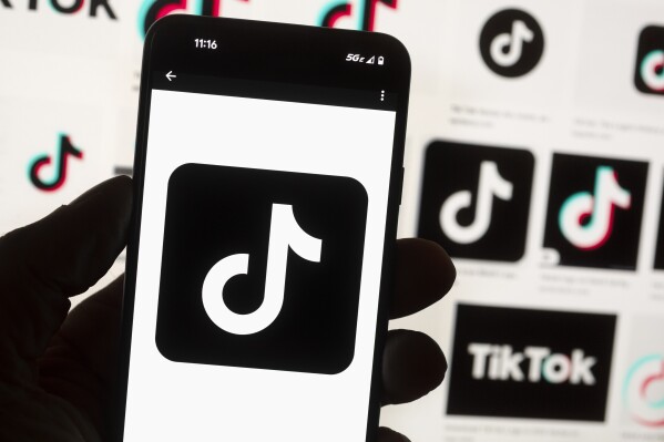 FILE - The TikTok logo is seen on a mobile phone in front of a computer screen which displays the TikTok home screen, Oct. 14, 2022, in Boston. Lawmakers in Georgia, early Friday, March 29, 2024, approved a bill that would require parental permission before children younger than 16 could sign up for social media accounts. (AP Photo/Michael Dwyer, File)