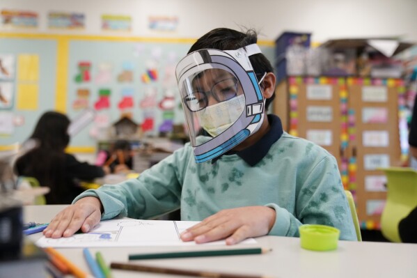FILE - A student wears a mask and face shield in a 4th grade class amid the COVID-19 pandemic at Washington Elementary School on Jan. 12, 2022, in Lynwood, Calif. Four years after the COVID-19 pandemic closed schools and upended child care, the CDC says parents can start treating the virus like other respiratory illnesses. (AP Photo/Marcio Jose Sanchez, File)