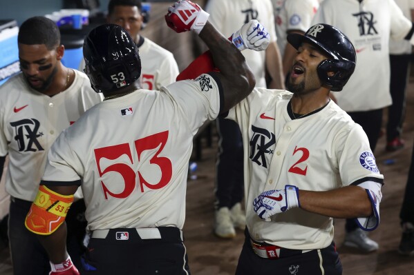 Texas Rangers' Adolis García (53) celebrates the home run by Marcus Semien (2) against the Cincinnati Reds during the eighth inning of a baseball game Friday, April 26, 2024, in Arlington, Texas. (AP Photo/Richard W. Rodriguez)