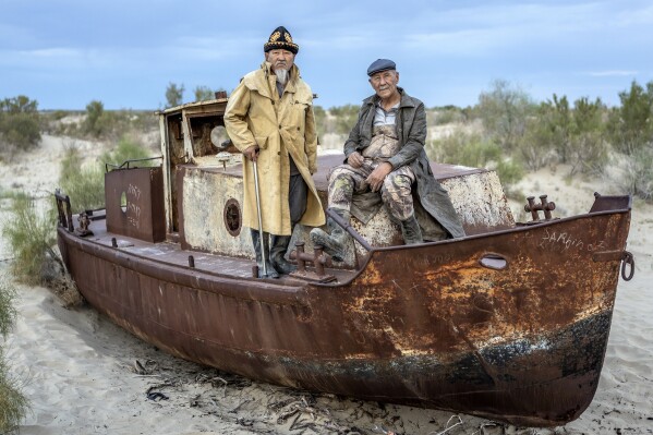 Ali Shadilov, left, and Anvar Saimbetov pose in front of an old boat in the area where the Aral Sea once was in Muynak, Uzbekistan, Tuesday, June 27, 2023. The Associated Press interviewed Shadilov and others in Muynak, Uzbekistan – all residents in their 60s and 70s who’ve long been tied to the sea, or what remains of it. (AP Photo/Ebrahim Noroozi)
