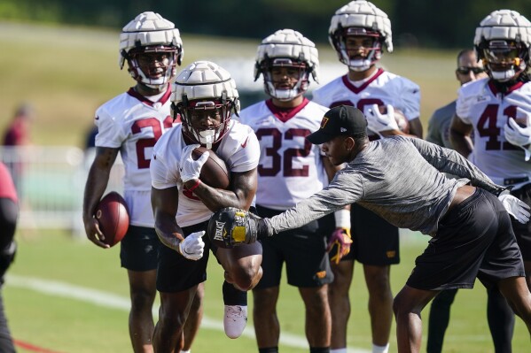 FILE - Washington Commanders running back Brian Robinson, second from left, wears a Guardian cap during practice at the team's NFL football training facility July 27, 2022 in Ashburn, Va. The NFL says will allow players to wear protective soft-shell helmet covers known as Guardian caps during games next season if they choose. The league is also expanding the use of the devices during practices. Defensive backs and receivers have joined the position groups now required to wear the caps during all contact practices. (AP Photo/Alex Brandon, File)