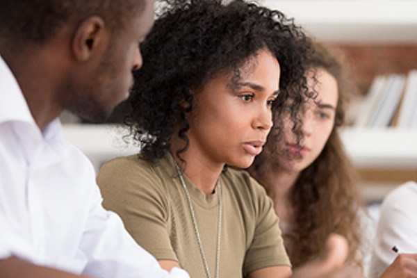 A woman sits in the foreground speaking while a woman and man sit to her right and left listening.