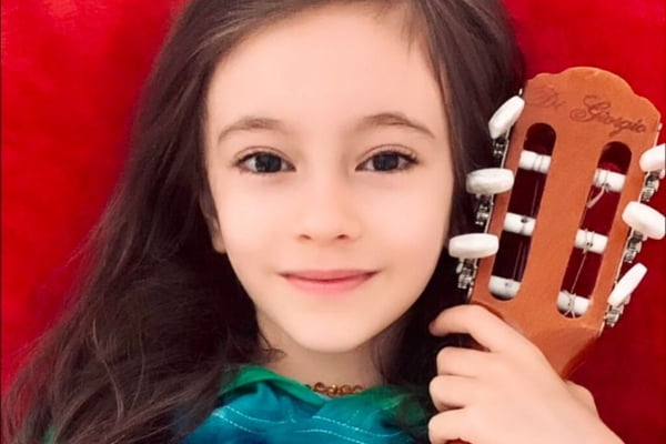 Foto colorida de uma menina branca, com cabelo castanho escuro, segurando um violão - Metrópoles