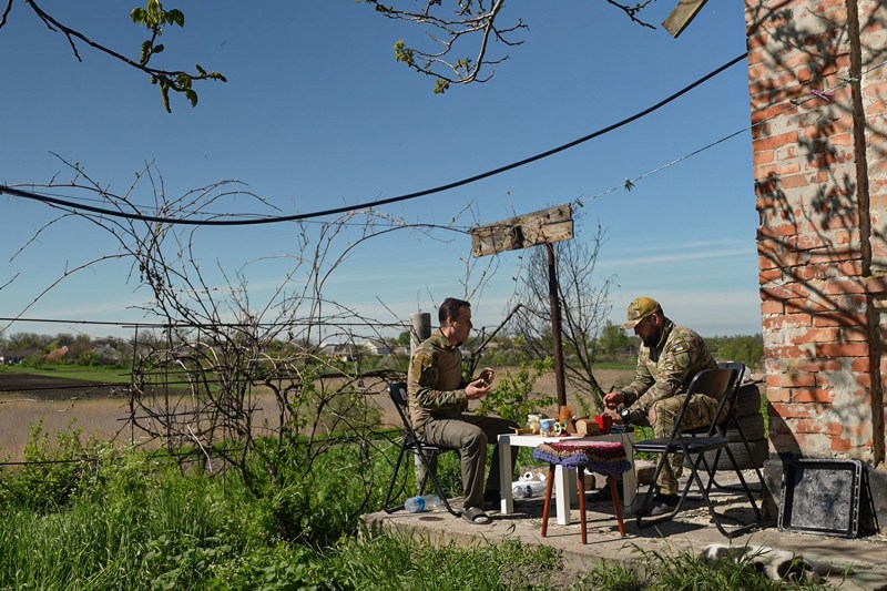 Two soldiers have breakfast outside at a small table next to their cottage near Avdiivka, Ukraine.
