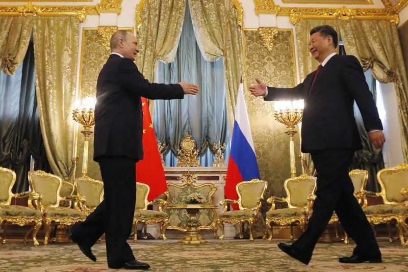 Russian President Vladimir Putin and Chinese President Xi Jinping reach out to shake hands, against a backdrop of Russian and Chinese flags, at the Kremlin in Moscow.
