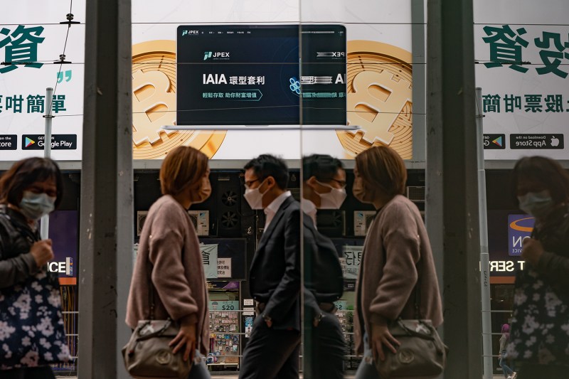 People walk by an ad with two Bitcoin cryptocurrency tokens.