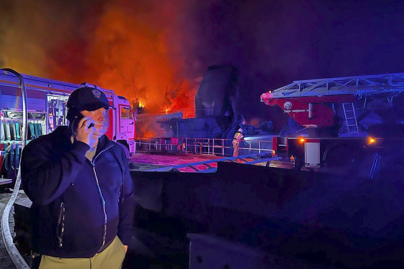 Sevastopol Gov. Mikhail Razvozhaev speaks on a mobile phone as smoke and flames rise behind him from the burning Sevastopol Shipyard in Russian-annexed Crimea at night after an attack by Ukraine. Also seen are fire-fighhting vehicles.