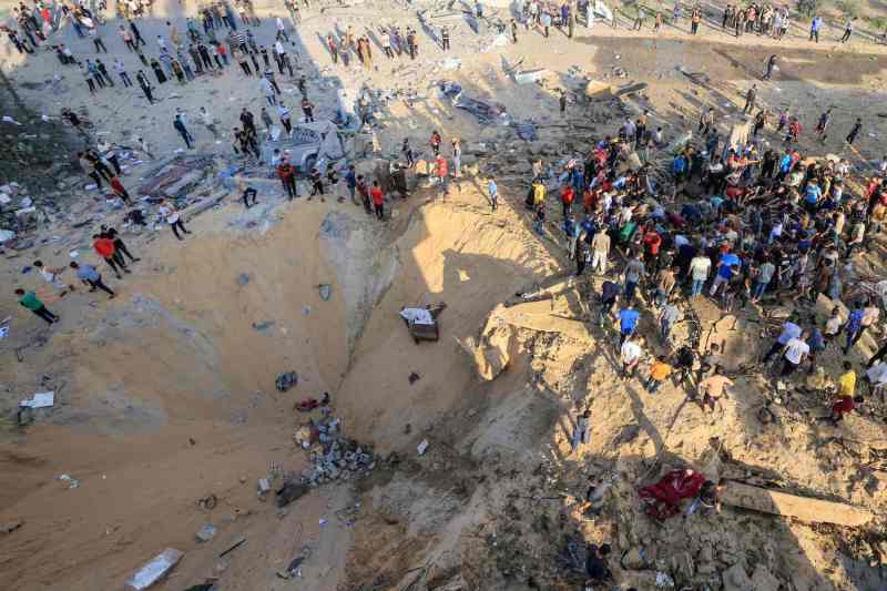 Palestinians stand next to a crater in southern Gaza.
