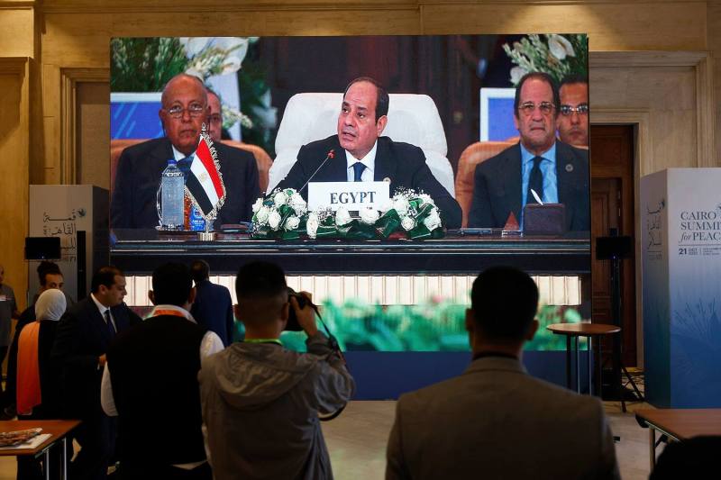 A large screen in a big conference center shows Sisi seated at a table alongside other officials.