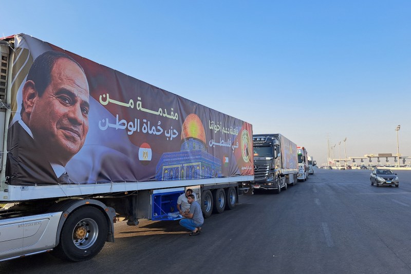 A convoy of trucks carrying aid supplies for the Gaza Strip from Egypt waits to cross into Gaza on the main Ismailia desert road on Oct. 16. A banner covering one truck displays a portrait of Egyptian President Abdel Fattah al-Sisi.