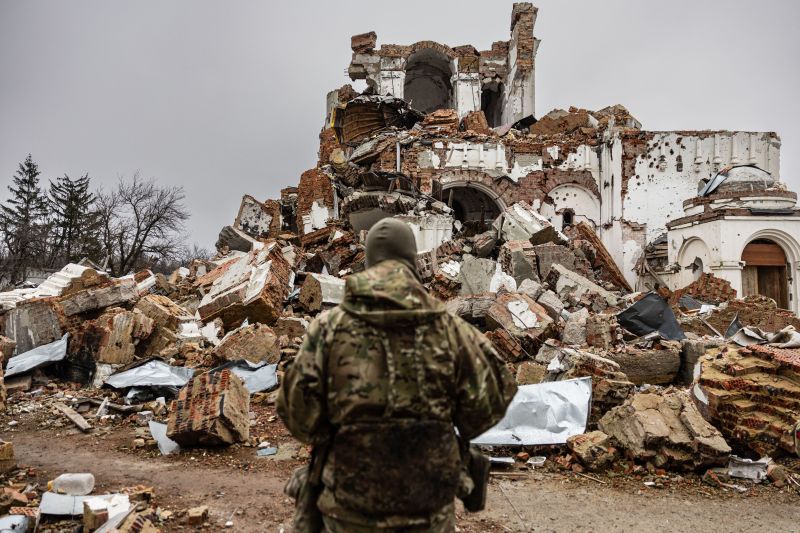 A soldier fighting for Ukraine stands in front of a destroyed monastery in Dolyna, Ukraine.