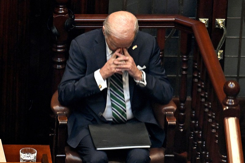 U.S. President Joe Biden puts his fingers to his eyes with his head bowed and hands clasped in prayer. A folder sits on his lap as he sits in the lower house of the Irish parliament.