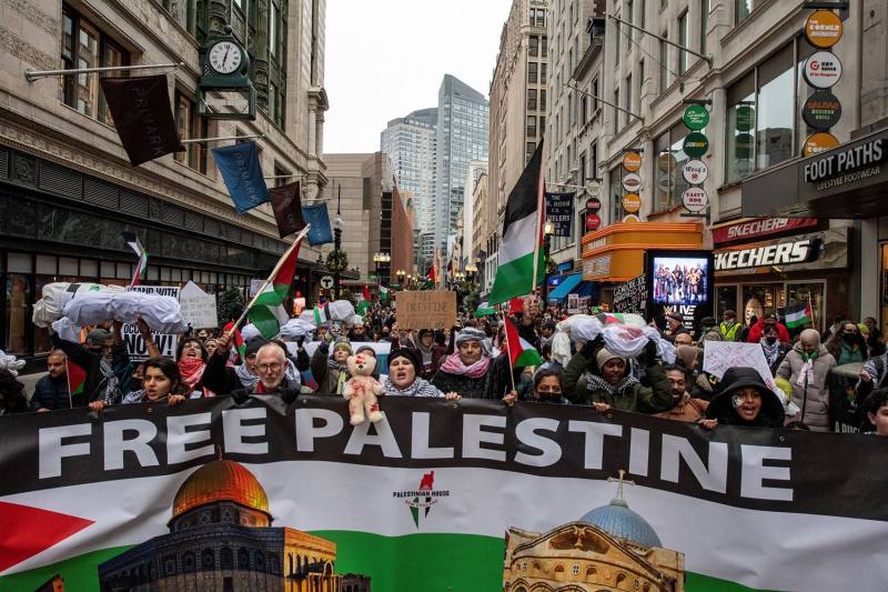 Demonstrators hold a large banner that reads "Free Palestine" as they march down a city street.