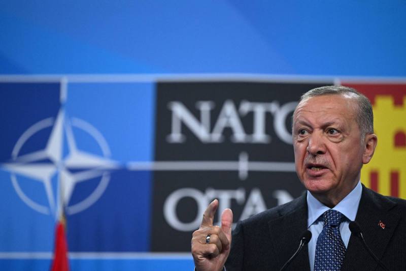 Erdogan gestures in the foreground in front of a backdrop featuring the NATO logo.