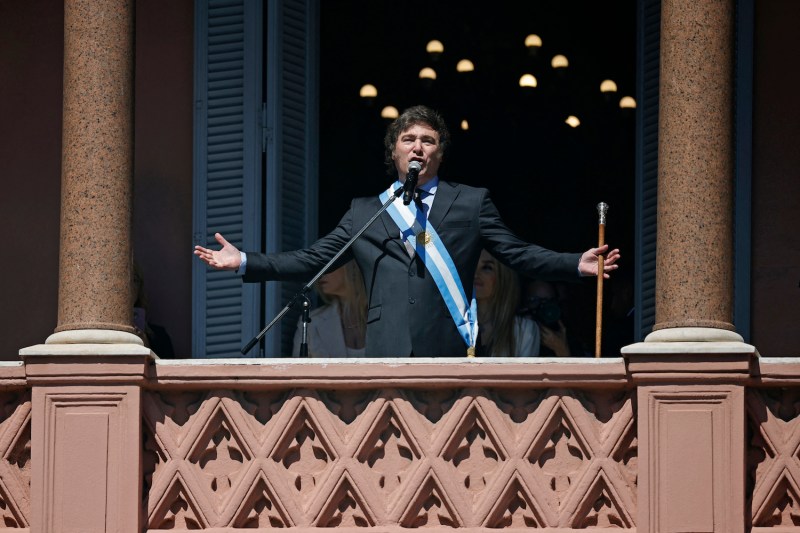 Milei spreads his arms out wide on a balcony, speaking into a microphone.