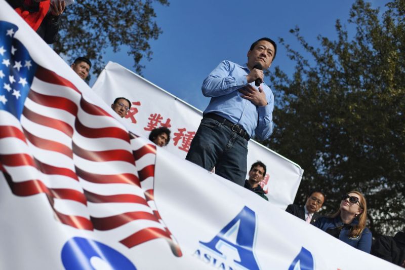 A man in a blue shirt stands behind a banner with an image of the U.S. flag.