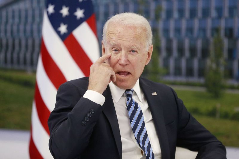 Biden scratches his eye in front of a U.S. flag.