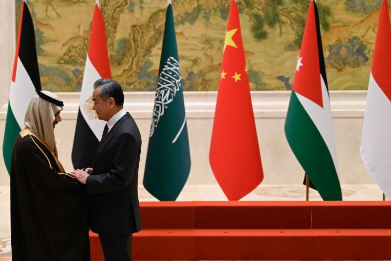 Chinese Foreign Minister Wang Yi shakes hands with Saudi Arabian Foreign Minister Prince Faisal bin Farhan Al Saud as the two man stand in front of a set of risers before a photo op at a diplomatic event hosted in an ornately decorated room in Beijing.
