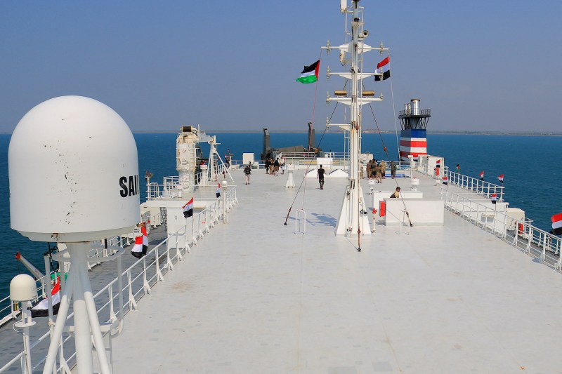 A picture taken during an organized tour by Yemen's Houthi rebels shows the deck of the Galaxy Leader cargo ship as it floats on the Red Sea beneath a hazy blue sky. Houthi fighters patrol the deck, and the Yemeni and Palestinian flags hang from the main mast.