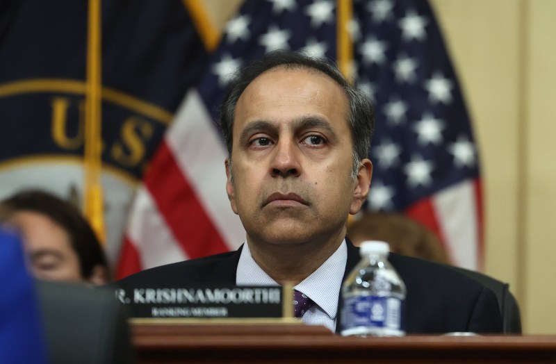 Rep. Raja Krishnamoorthi sits at a desk behind his nameplate during a select committee meeting at the House of Representatives. Krishnamoorthi is a middle-aged man with a serious expression, wearing a black suit and purple tie.