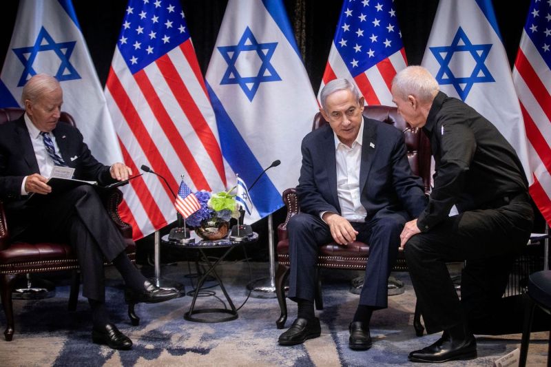 Israeli Prime Minister Benjamin Netanyahu and Defense Minister Yoav Gallant speak during a meeting with U.S. President Joe Biden in Tel Aviv. Israeli and U.S. flags hang in the foreground.