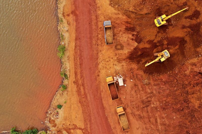 Excavators and trucks involved in a nickel mining operation are seen from above next to a river in Indonesia.