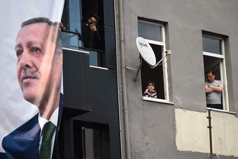 Local residents listen to the Turkish President's speech next to his a banner with his portrait during a rally in the Beyoglu district on the eve of the presidential and parliamentary elections, on the European side of Istanbul, on May 13, 2023. Images)