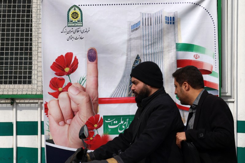 Men ride their scooter in front of a poster encouraging Iranians to vote in the upcoming elections, in Tehran.