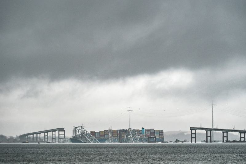 The Dali, a Singapore-flagged cargo ship that is almost as long as three football fields, remains stuck under debris from the collapsed Francis Scott Key Bridge in Baltimore Harbor under a cloudy gray sky.