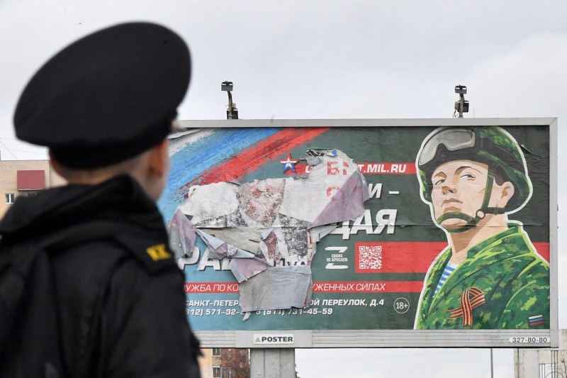 A military cadet stands in front of a billboard promoting contract army service in St. Petersburg.