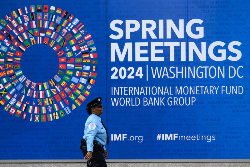 A security guard walks past a large blue banner that says SPRING MEETINGS 2024 | WASHINGTON DC INTERNATIONAL MONETARY FUND WORLD BANK GROUP.