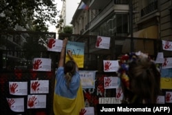 Украинцы и аргентинцы, протестующие против войны, приклеивают листовки к забору, ограждающему посольство России в Буэнос-Айресе. 1 марта 2022 года