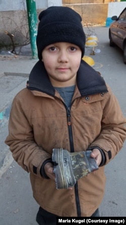 Сын Саши и Наташи держит в руках осколок российского снаряда, взорвавшегося возле их дома